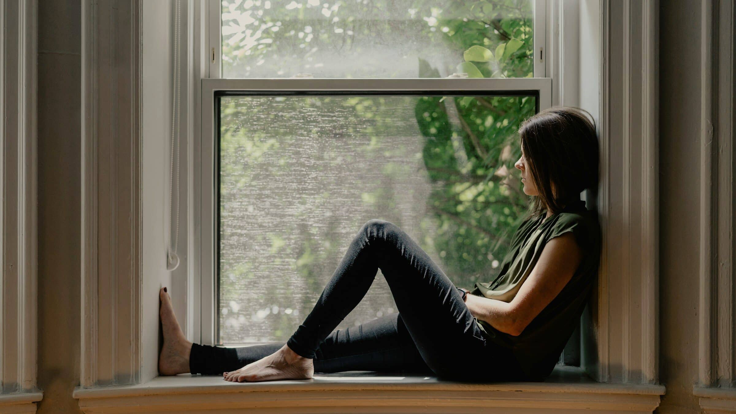 Mujer sentada junto a una ventana al amanecer, ojos cerrados, bañada en luz natural cálida