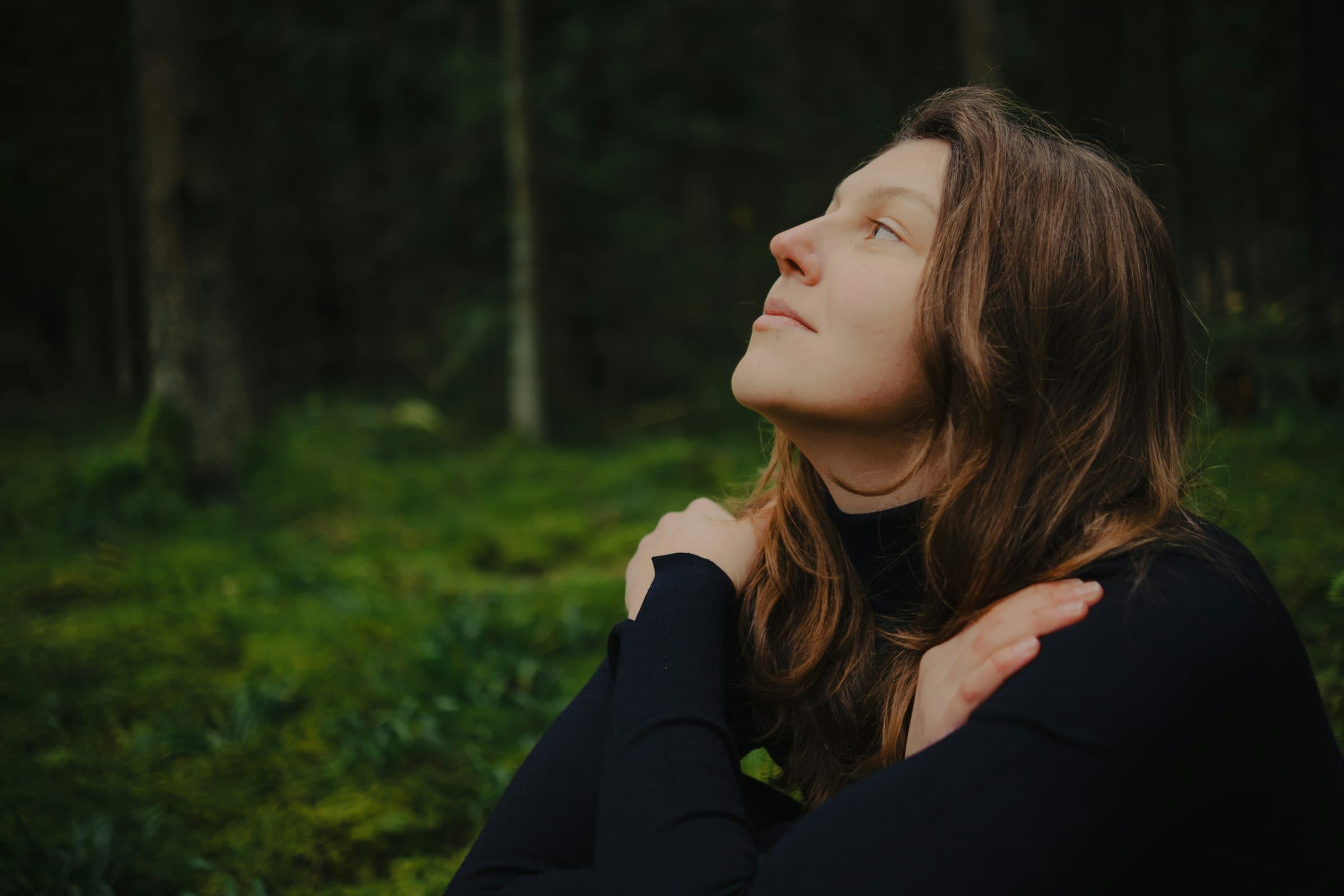 Una mujer sentada en una postura serena, respirando profundamente en un entorno natural tranquilo.