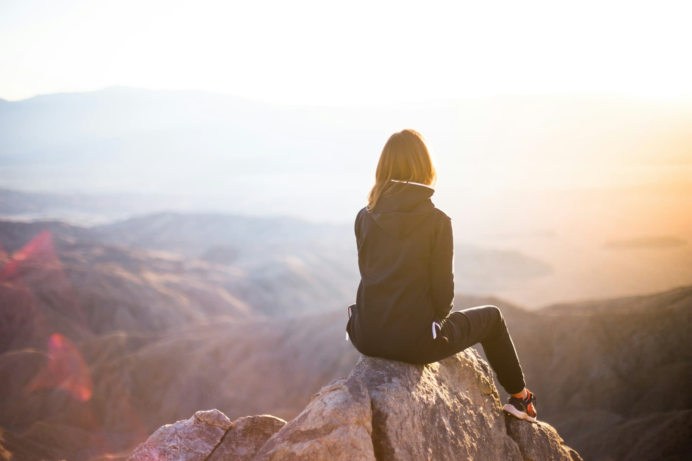 Una mujer meditando tranquilamente en un paisaje natural al amanecer, simbolizando paz y conexión.