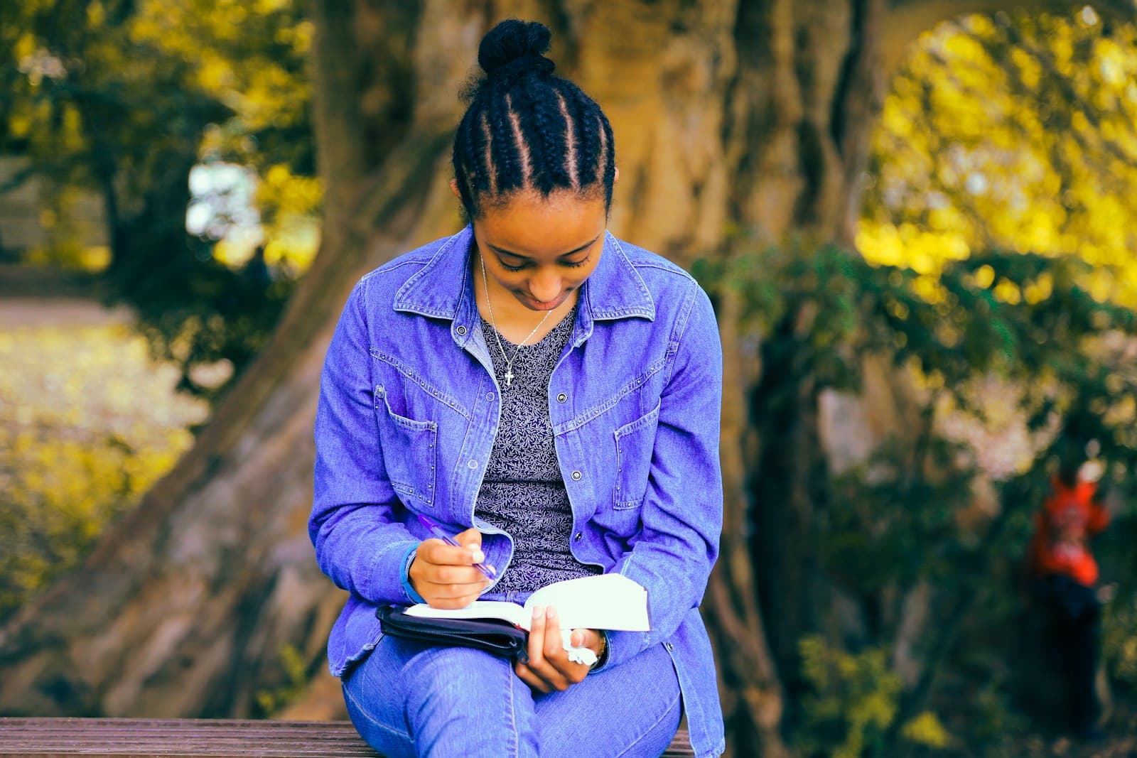 Una persona escribiendo en un diario al aire libre, con la naturaleza de fondo