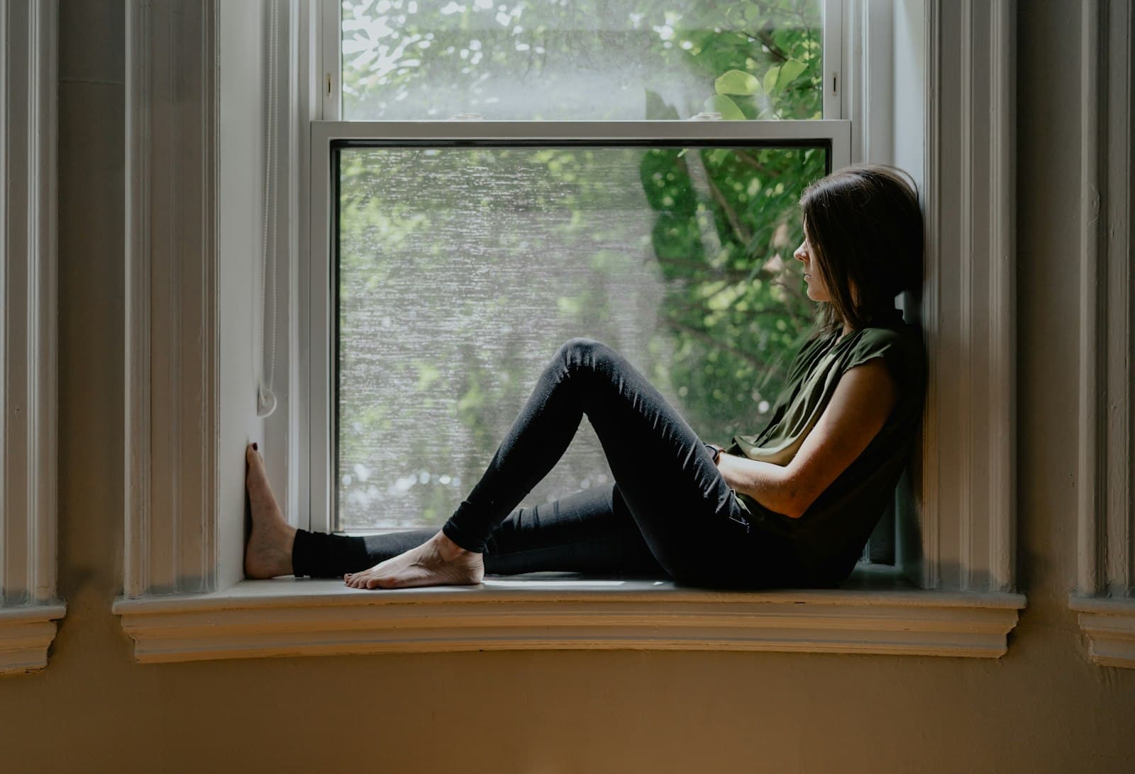 Una persona sentada tranquilamente junto a una ventana, disfrutando de un momento de calma y atención plena.