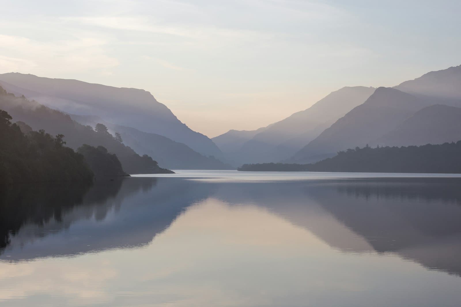 Un lago en calma al amanecer con reflejos de las montañas y el cielo