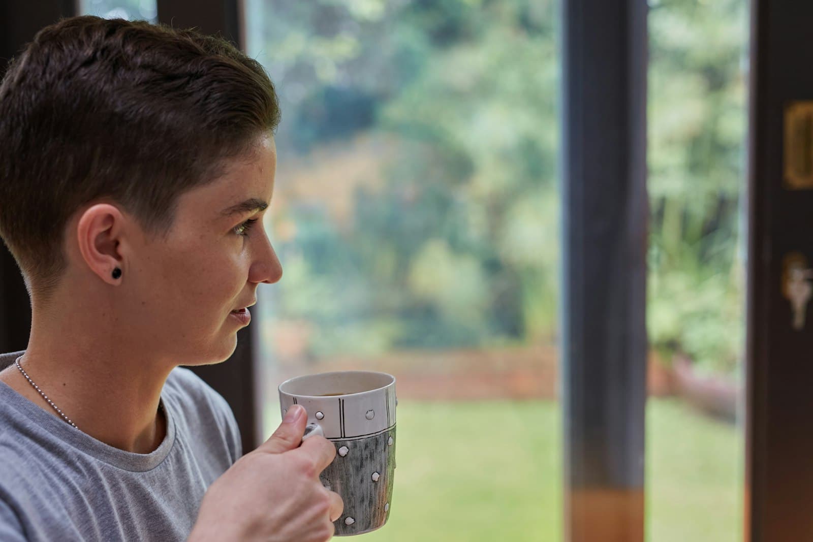 Una persona sosteniendo una taza de té caliente, mirando por una ventana con calma matutina